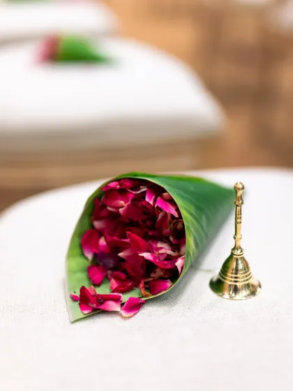 A close up detail shot of a cone made of leaves, filled with rose petals for guests to shower on the couple, next to a small brass bell.