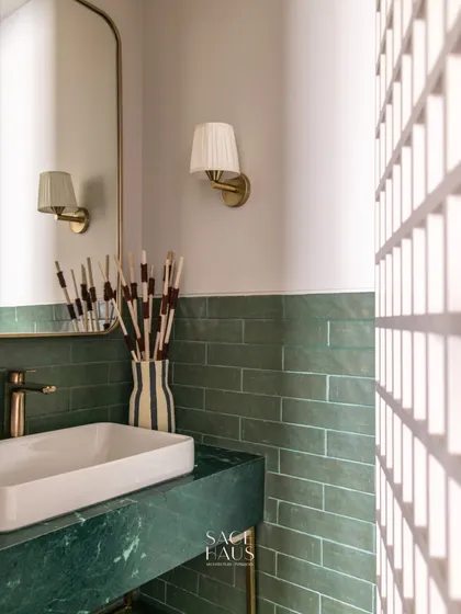 I love playing with color and texture in a powder room. Here, a rich green marble vanity and green subway tiles are paired with a striped vase and a pleated wall sconce for a look that is fresh, modern, and full of character.