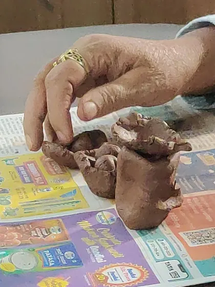 A senior's hand reaches for a small clay creation. The simple act of touching and manipulating the clay provides valuable sensory input and can help evoke memories and stories.