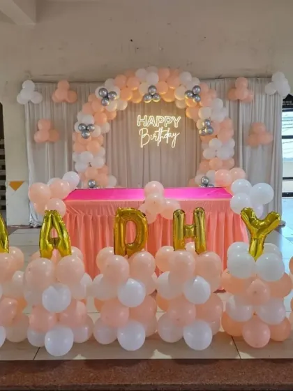 A peach and white balloon arch with personalized letter balloons spelling "AADHYA".
