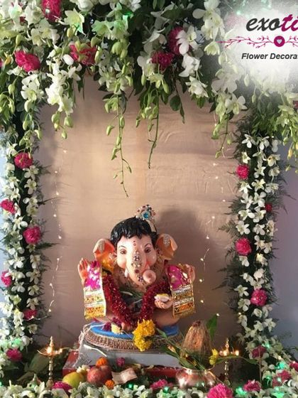 A delicate and charming Ganpati decoration featuring a canopy of white and pink orchids with gentle, hanging vines. The soft lighting and fresh flowers create an ethereal and welcoming space for the idol.