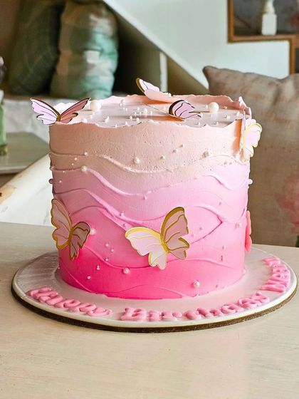 An elegant ombre cake transitioning from white to deep pink, decorated with delicate wafer paper butterflies.