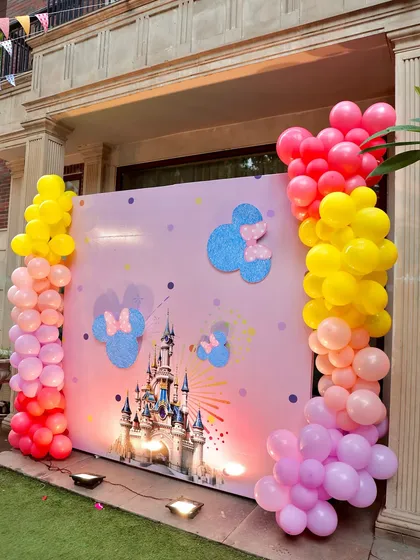 A beautiful pink backdrop for a Disney-themed party, featuring the iconic castle and glittery Mickey Mouse head silhouettes. The ombre balloon columns add a modern and colorful touch.