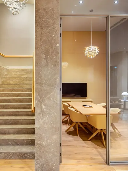 A view into a meeting room from a marble-clad staircase area. The design uses glass walls to maintain a sense of openness and connection between different functional zones.