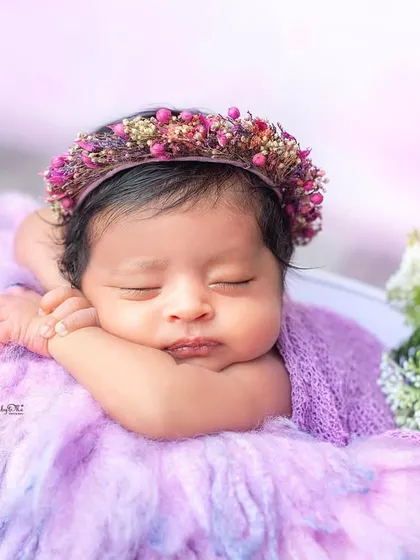 A beautiful sleeping portrait of a newborn girl wearing a floral crown. The shades of purple and the soft textures make this image feel like a fairytale.