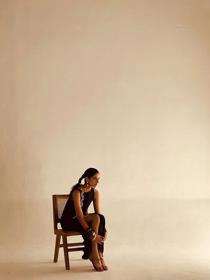 Minimalism with an edge. A model sits in a simple black dress with a side slit, styled with bold, chunky bracelets for an avant-garde touch.