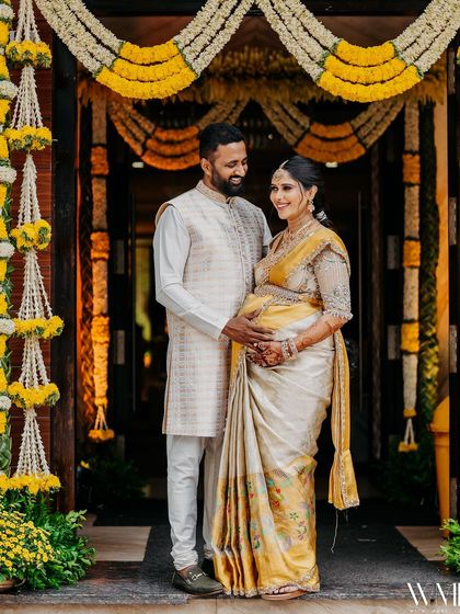 A full-length shot of my husband and me at my baby shower. The floral decorations provide a beautiful backdrop for our coordinated traditional wear.