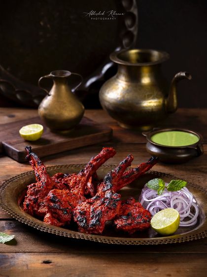 Barbecue lamb chops for The Nawaab’s, Hyderabad. The moody lighting and dark wood background create a dramatic effect, emphasizing the perfectly grilled meat.