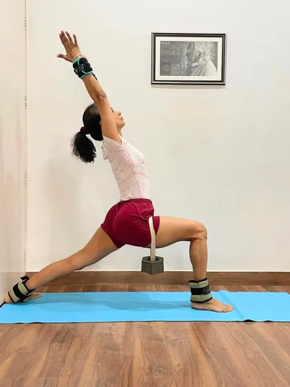 Virabhadrasana I (Warrior I) is shown here with weights on the ankles and wrists. The weights add resistance, helping to build strength and stability, and also provide grounding energy to the pose.