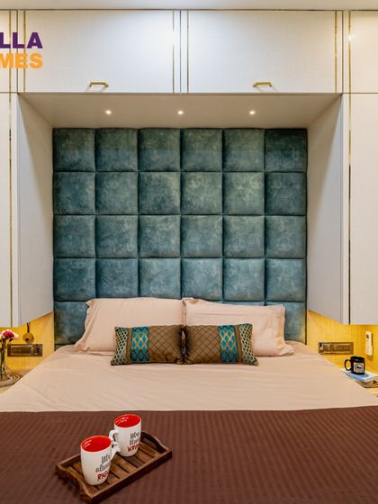 A front view of the bed with its tufted teal headboard, flanked by custom wardrobes with integrated bedside niches and warm lighting.
