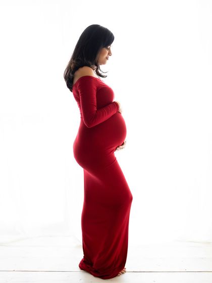 A side profile silhouette against a bright white background. The vibrant red gown creates a powerful and striking image that beautifully accentuates her baby bump.