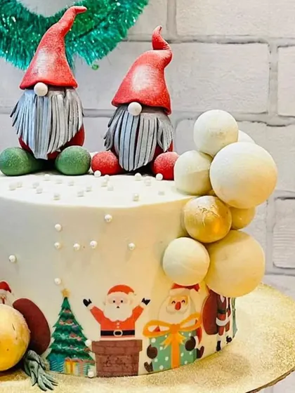 A whimsical Christmas cake featuring two adorable gnomes. The cake is decorated with edible printed scenes of Santa and his reindeer, adding a playful touch to your celebration.
