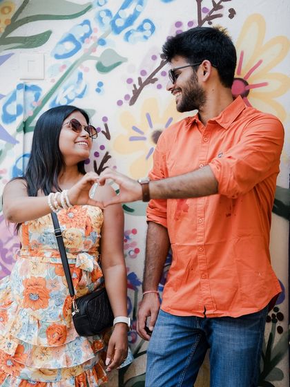 A sweet pose in front of a vibrant floral mural in Goa, with the couple making a heart shape with their hands.