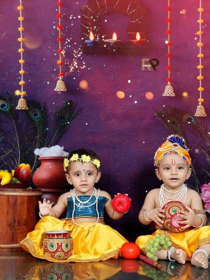 A beautiful portrait of two babies dressed as Radha and Krishna, sitting together in a festive setup. This is a wonderful way to capture siblings or friends celebrating together.