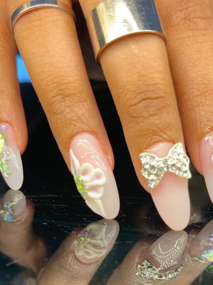 A close-up of the intricate 3D nail art, featuring a rhinestone bow, sculpted flower, and iridescent gems.