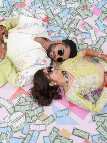 A cool, creative shot of the couple lying on a bed of custom-printed money, perfectly capturing the fun and quirky vibe of their carnival.