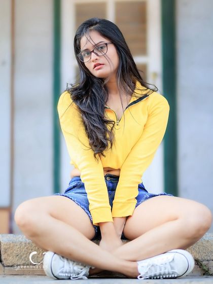 A cool and casual seated pose. The addition of glasses adds a touch of intellectual chic to the look.