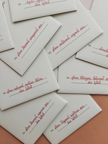 A collection of envelopes addressed in Gujarati script. The red ink provides a beautiful contrast against the white paper, creating a traditional and elegant look.