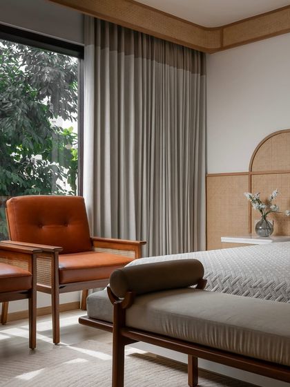 The guest bedroom at Haus of Aureus features a custom bed with a cane and wood arched headboard. We added a pop of color with burnt orange leather armchairs, creating a warm and inviting corner.