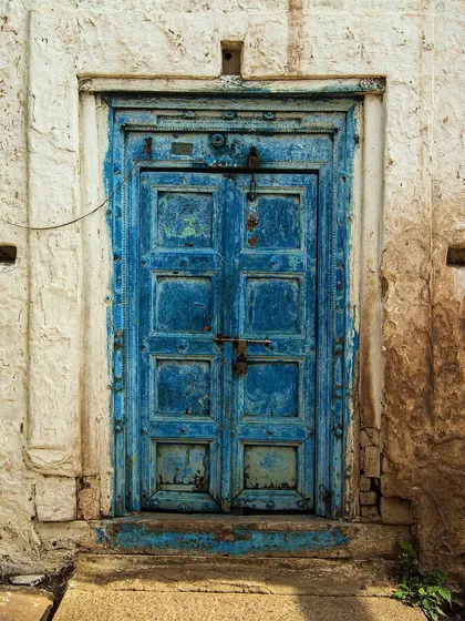 This heavily textured blue door shows years of wear, with layers of paint peeling away to reveal the wood beneath. The rustic locks and bolts add to its vintage, authentic character.