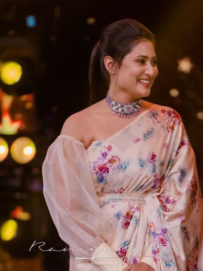 Actress Amrutha Iyengar in a bespoke flowy floral satin saree, designed with a modern off-shoulder blouse and an embellished pearl belt for a red-carpet look.