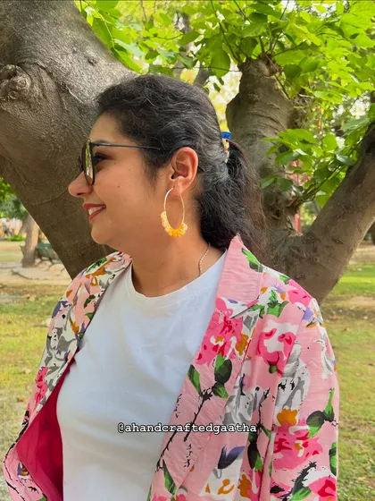 A customer looking radiant in the sunflower yellow 'Naazakat' hoops. They're the perfect accessory to pair with a floral blazer for a cheerful, coordinated look.