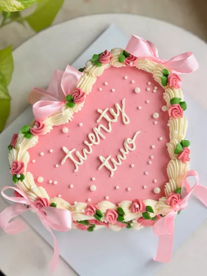 A beautiful overhead shot of the pink heart-shaped cake for a 22nd birthday, detailed with buttercream roses, pearls, and satin bows.