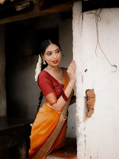 A beautiful portrait of a model in a traditional saree, framed by a weathered wall. Her pose and the setting evoke a sense of nostalgia and timeless grace.