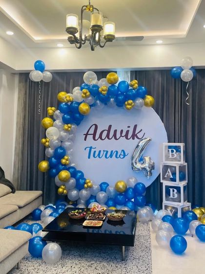 A blue and gold themed 4th birthday for "Advik" in a living room. The setup includes a custom circular backdrop, a balloon arch, and "BABY" blocks, creating a complete party look.