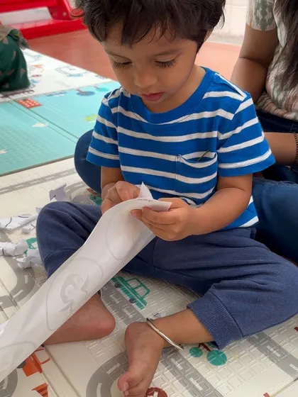 A child practices tearing paper along a line, a pre-scissor skill that builds hand strength and coordination. It's all part of our play-based approach to skill development.