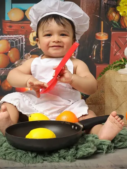 Who needs a recipe when you have this much cuteness? This little chef is having a blast playing with a pan and lemons in a kitchen-themed setup, perfect for a one-year-old's photoshoot.