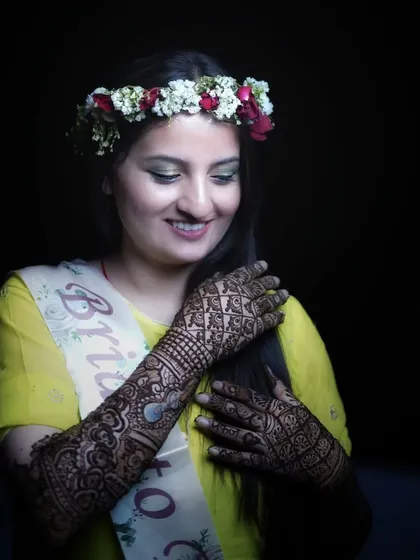 A close up portrait of the bride wearing a "Bride to Be" sash and a floral crown. This shot focuses on her happy expression and the detailed mehendi art.