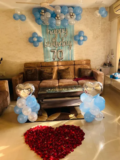 A full view of the 70th birthday home decoration. The living room is decorated with blue and silver balloons, foil hearts, and a large rose petal heart on the floor.