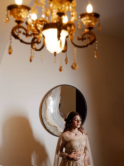 A stunning portrait of the bride under a golden chandelier. The warm lighting and her elegant pose create a luxurious and glamorous pre-wedding shot.