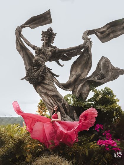 A stunning solo portrait of the bride-to-be in Bali, with her flowing pink dress mimicking the movement of the statue behind her. This is a perfect example of artistic and creative pre-wedding photography.