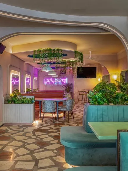 The interior of Hangover uses a pastel color palette of dusty rose and teal. Curved booth seating, arched mirrors with neon lighting, and hanging plants create a soft, playful, and inviting atmosphere.
