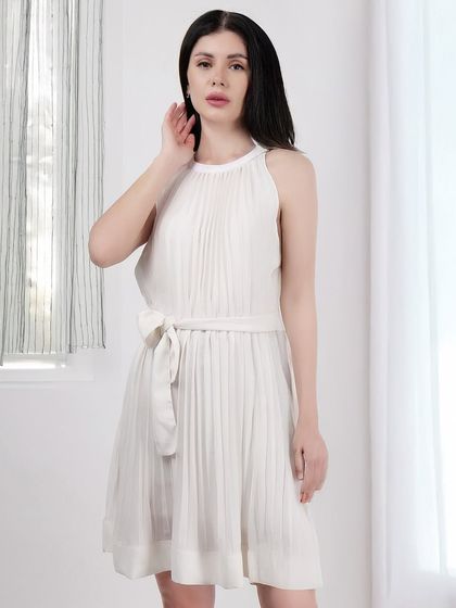 A model in an elegant white pleated dress, captured with soft, bright lighting to emphasize the garment's texture and flow.