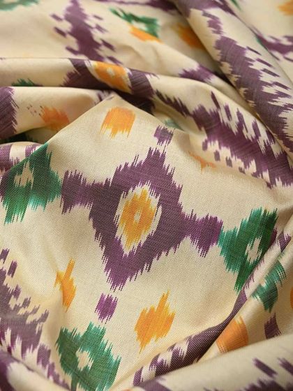 A close-up of a silk Ikkat fabric, showing the characteristic blurred edges of the pattern that result from the resist-dyeing process. The colors are vibrant and beautiful.