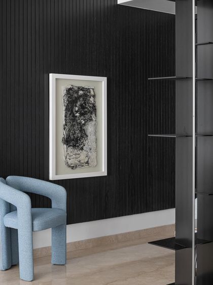 Even transitional spaces like a foyer can be a place for art. Here, a bold, sculptural chair in a striking blue is set against a black fluted wall with abstract art, creating a powerful and memorable first impression.