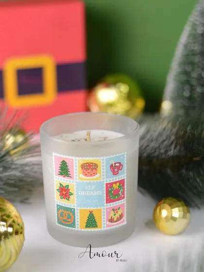 The 'Elf Dreams' jar candle features cute stamp-like designs and a sweet chocolate and vanilla fragrance.