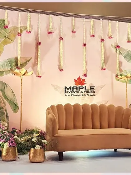 A tropical-themed stage design with large banana leaf prints on the backdrop and fresh floral arrangements. The hanging floral strings and golden pots add a touch of elegance to this fresh and vibrant setup.