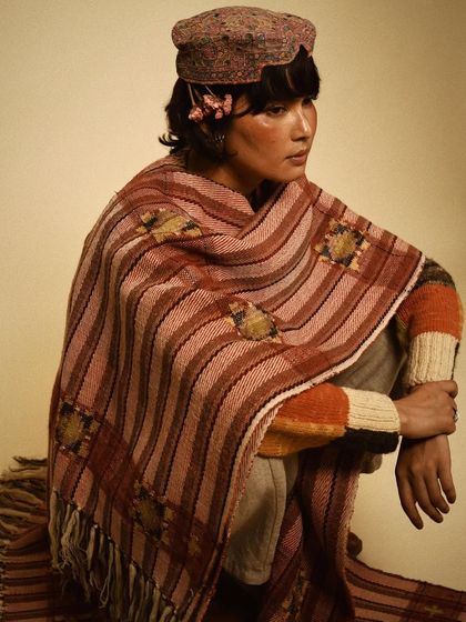 A seated portrait for House of Wandering Silk, showcasing a stunning woven shawl. The composition is grounded and highlights the craftsmanship of the piece.