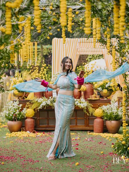 A bride strikes a pose with her flowing dupatta against a stunning backdrop of yellow marigold decor.