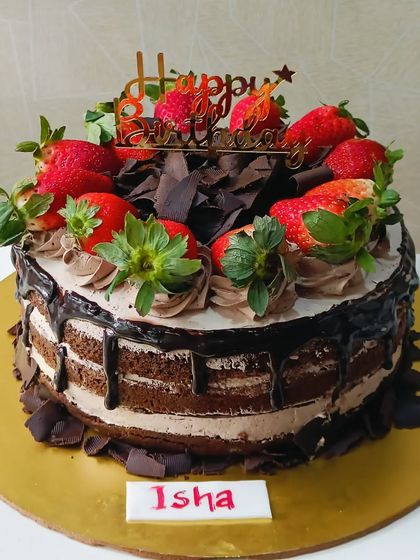 A rustic chocolate and strawberry cake. The layers of chocolate cake and cream are topped with a chocolate drip, chocolate shavings, and plenty of fresh strawberries.