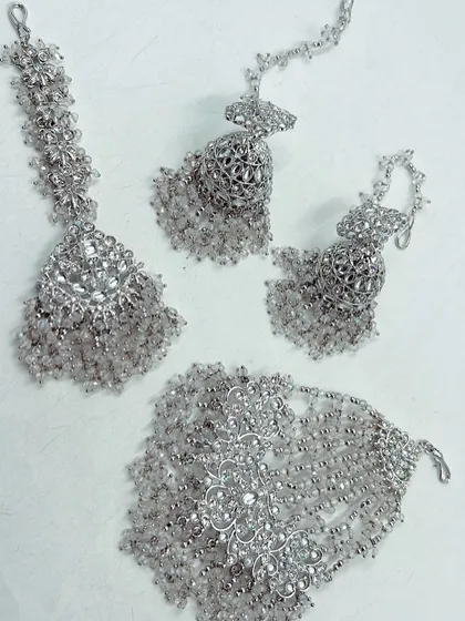 A stunning silver-toned jewellery set with clear beads, ideal for a modern Haldi or Mehendi look. This rental set includes a maang tikka, hathphool, and earrings.