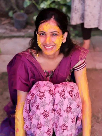 A bright and happy portrait of the bride during her Haldi. Her face is covered in turmeric, and her smile is infectious, showing the pure joy of the moment.