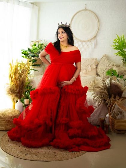 A wide shot of our boho studio setup, featuring a mom-to-be in a gorgeous red ruffled gown. This image showcases the beautiful environment we create for our sessions.