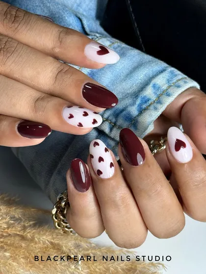 A romantic and chic design with deep dark maroon nails paired with a milky white base and tiny, hand-painted hearts. This look is perfect for a date night or any time you want to feel gorgeous.