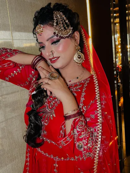 A stunning Pakistani bridal look, rich in tradition and elegance. This style features a vibrant red outfit, elaborate gold jewelry including a jhoomar and passa, and dramatic eye makeup with a flawless base, capturing the grandeur of a traditional Nikah ceremony.