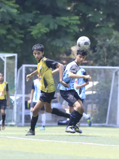 A player uses his head to control the ball, battling for aerial dominance against an opponent. This highlights the importance of aerial skills in a match.